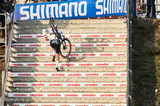 Mathieu van der Poel shoulders his bike up a long flight of sponsor-branded steps beneath a Shimano banner at Hoogerheide.