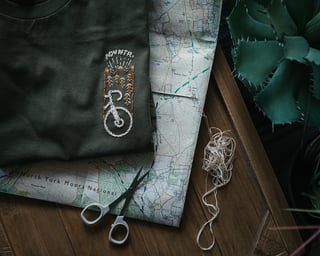 Get Wild x ADVNTR t-shirt with the coffee and cream embroidered bike motif, lying on a North York Moors map.