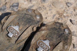 Worn soles of the Fizik Terra X5 with silver SPD cleats caked in mud and dust.