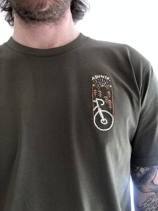 Man wearing the army green Get Wild x ADVNTR t-shirt with the embroidered bike motif on the left breast.