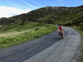 TransAtlantic Way Race rider on a Brompton cycles a narrow road through steep green hills in Donegal.