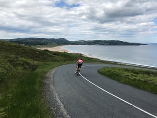Brompton rider descends a hairpin bend towards a sandy beach and bay on the Donegal coast.