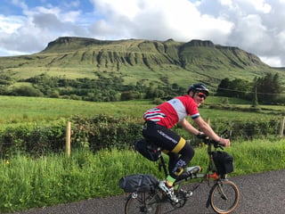 Smiling rider on a loaded Brompton passes the green flat-topped slopes of Ben Bulben in County Sligo.