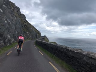 Rider on a Brompton follows a coastal road along a dry-stone wall above the Atlantic in Kerry.
