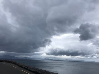 Heavy grey clouds over the sea beside a stone-walled coastal road on the TransAtlantic Way in south-west Ireland.