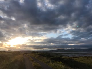 Low sun breaks through heavy cloud over a narrow coastal track and tidal estuary on the TransAtlantic Way.