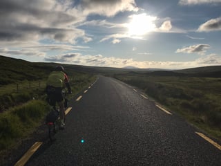 Brompton rider seen from behind on an empty Irish moorland road in low evening sun during the race.