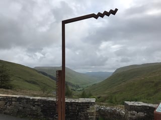 Rust-coloured sculpture marking Glengesh Pass above a green valley on the TransAtlantic Way route in Donegal.