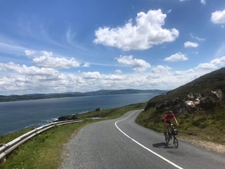 A Brompton rider climbs a quiet coast road above a sea inlet during the TransAtlantic Way Race in Donegal.
