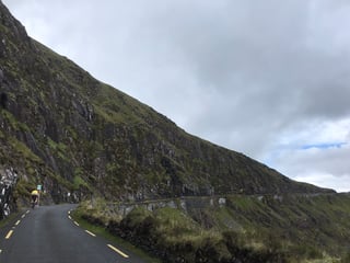 Distant cyclist on a narrow road below a steep, rocky hillside on the Kerry stage of the TransAtlantic Way.