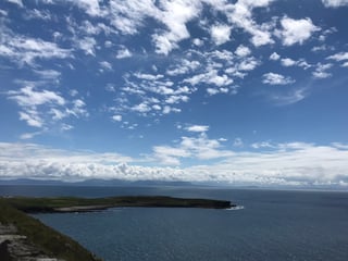 Blue sky over a dark headland and open Atlantic, with distant mountains on the Wild Atlantic Way coast.