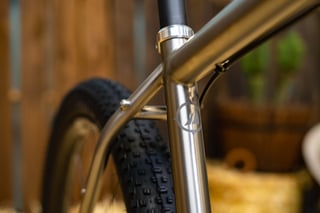 Seat tube junction on the Bingham Built Adventure titanium frame, with a compass-style logo and a Plus tyre behind.
