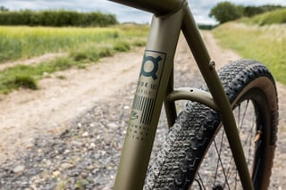 Bombtrack Hook EXT size large decal on the matte olive seat tube, with a tan-wall Teravail tyre beside a farm track.