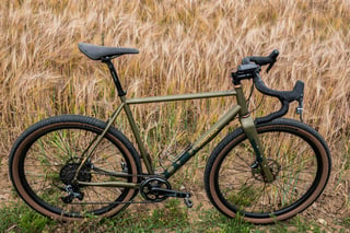 Side view of the matte olive Bombtrack Hook EXT with tan-wall Teravail tyres against ripe barley.