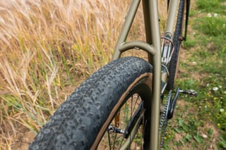 Teravail Sparwood tyre on the Bombtrack Hook EXT's olive steel frame, beside a field of barley.