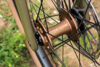 Chris King R45 front hub in matte bourbon, laced with black spokes on the Bombtrack Hook EXT.