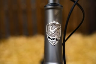 Moots head badge, a cartoon reptile riding a bike beneath mountains, on the Routt 45's titanium head tube.