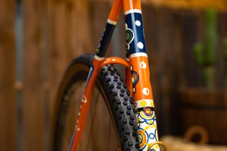 Hand-painted orange and navy seat tube and seatstays on the Scarab Páramo, with a knobbly gravel tyre behind.