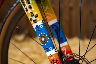 Painted fork leg on the Scarab Páramo in blue, yellow and orange, with white and black dot patterns.