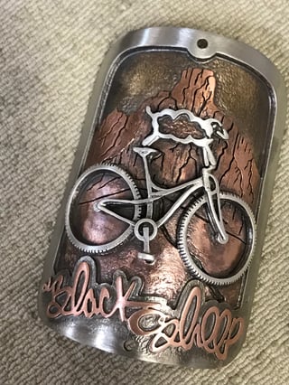 Jen Green mixed-metal head badge of a sheep riding a mountain bike before copper mountains, with Black Sheep lettering.