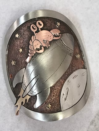 Jen Green head badge in silver and copper of a lobster riding a rocket past the moon and stars.