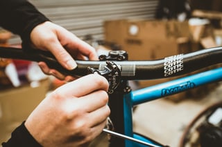 Hands tighten a lever clamp beside the stem on the new Cotic flat bar of the blue Escapade.