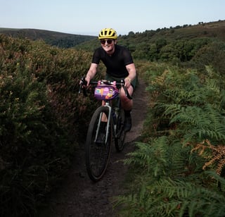 Smiling rider in a yellow helmet rides the Temple Adventure Disc 1 along a bracken-lined Quantock Hills singletrack.