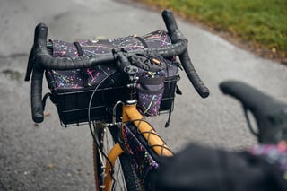 Wizard Works splatter-fabric Alakazam basket bag in a Wald basket on the Faran's handlebars, on a wet path.