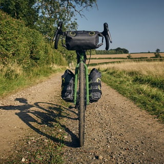 Front view of the Apidura-equipped Fairlight Faran, with a handlebar pack and two fork packs on a gravel lane.