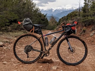 Muddy gravel bike with bikepacking bags on a red dirt forest track, snowy mountains in the distance.