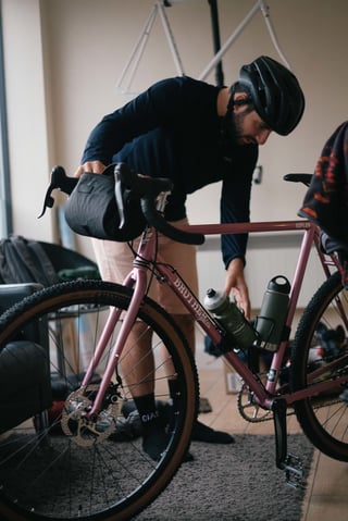 Rider leans over the pink Brother Cycles Kepler indoors, checking the bottle cages before setting off on the Kent ride.