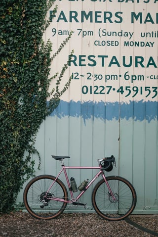 Pink Brother Cycles Kepler with bottle cages leaning against the painted Farmers Market sign at The Goods Shed, Canterbury.
