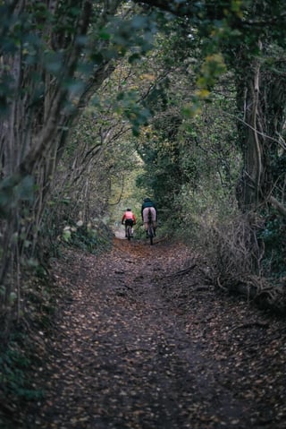 Two riders on gravel bikes head down a leaf-strewn sunken lane in Kent on the Brother Cycles recce.