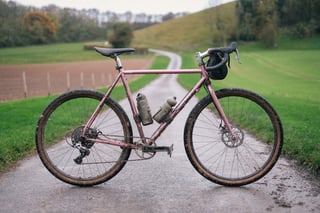 Stefan's mud-spattered pink Brother Cycles Kepler with bar bag and 650b Teravail Rutland tyres on a wet Kent lane.