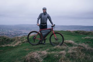 Rider stands behind a red bike with a full frame bag on the Wye Downs hilltop during the Brother Cycles Kent recce.