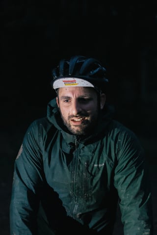Mud-flecked rider in a Pannier cap and green jacket, lit against the dark at the pub stop on the Brother Cycles Kent ride.