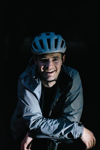 Smiling rider in a grey jacket and helmet, lit against a black night background at the pub stop in Kent.