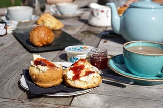 Cream tea with split scones, jam, cream and a pot of tea on a wooden table, a stop on the Quantock Hills ride.