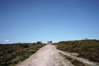 Three gravel riders head up a stony track between purple heather under a clear blue sky on the Quantock Hills.