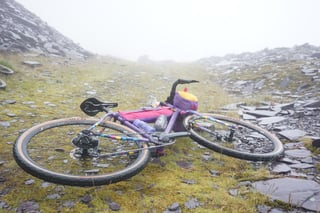 Loaded gravel bike with tan-wall tyres lying on a slate-strewn mountain track in thick mist.