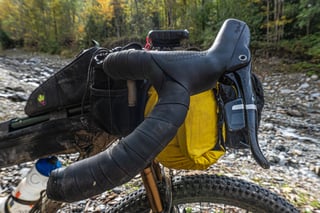 Close-up of the Curve Walmer drop bar with SRAM shifter, bar tape and handlebar bag on a river gravel bank.