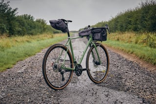 Woodland Green Fairlight Faran 2 with Gramm Tourpacking bags on a wet gravel track between hedges.