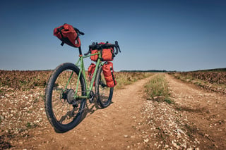 Fairlight Faran in Woodland Green with rust-orange Road Runner bags, parked on a chalky farm track.