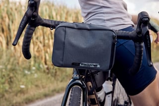 Rider on a gravel bike with the new PRO Discover handlebar bag strapped to the bars, beside a tall crop field.