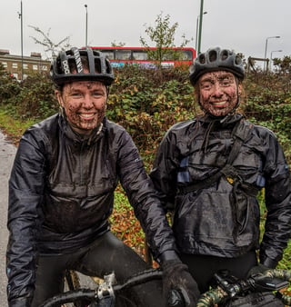 Two smiling riders with mud-spattered faces and jackets after a wet Stayer Groadinger UG test ride in Epping Forest.