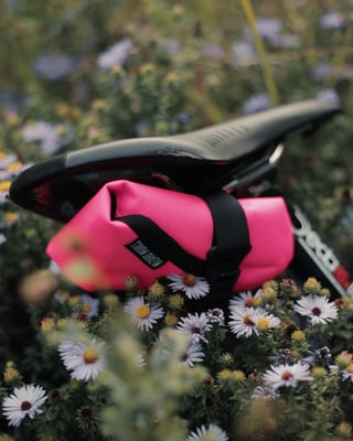 Wizard Works Teeny Houdini tool pouch in pink strapped under a saddle among wildflowers.