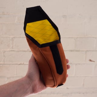 Hand holding the open rust Teeny Houdini, showing its yellow lined interior and Velcro closure tab.