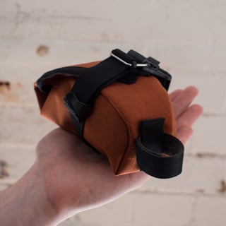 Rust Teeny Houdini held upside down in a hand, showing the underside strap, buckle and webbing loop.