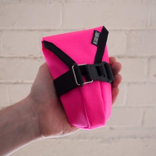 Small Teeny Houdini tool pouch in fluro pink, held in a hand against a white brick wall.