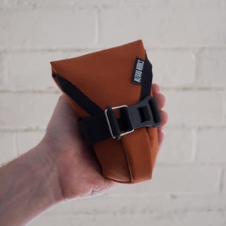 Small Teeny Houdini in the rust colourway, held in a hand with the Fidlock buckle fastened.